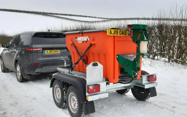 A wessex polar one salt and grit spreader, painted in orange, is parked on the roadside with a vast, snowy landscape in the background.